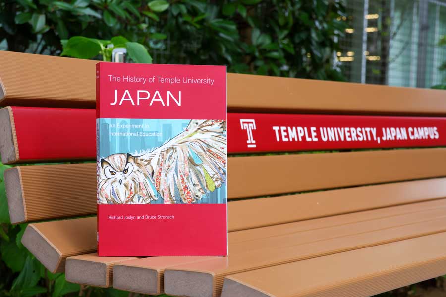 Copy of “The History of Temple University Japan: An Experiment of International Education” book. The cover of the book features a mural of the Parliament student lounge that has become a symbol of TUJ. Photo by William Galopin